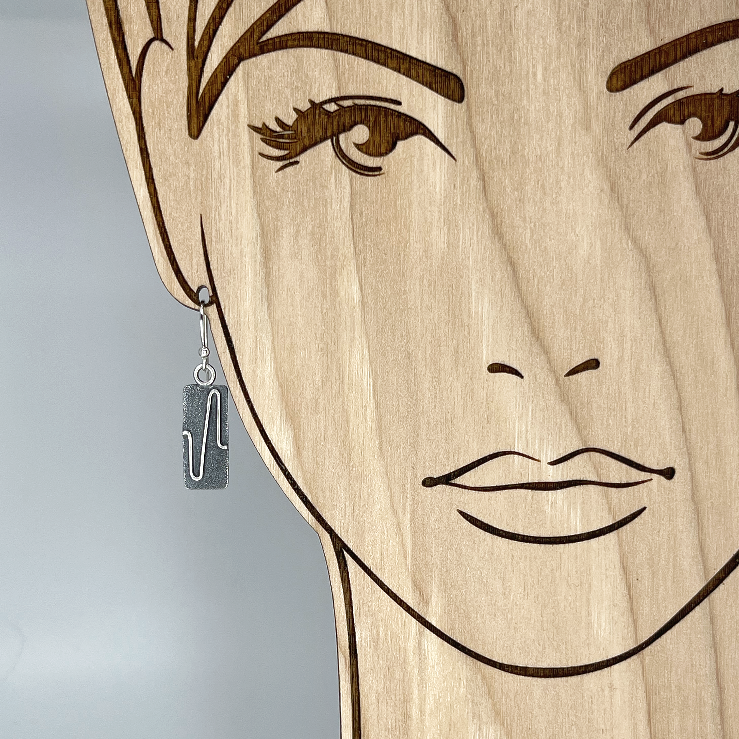 A rectangular sterling silver earring shown on a model