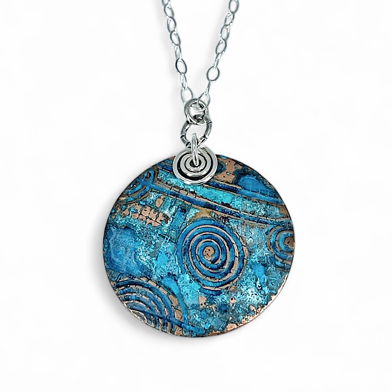 Front view of circular copper blue patina pendant with sterling silver chain and accents
