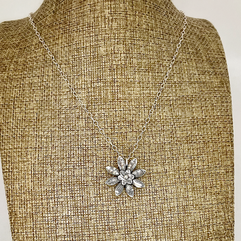 Silver necklace with a floral pendant on a mannequin bust.
