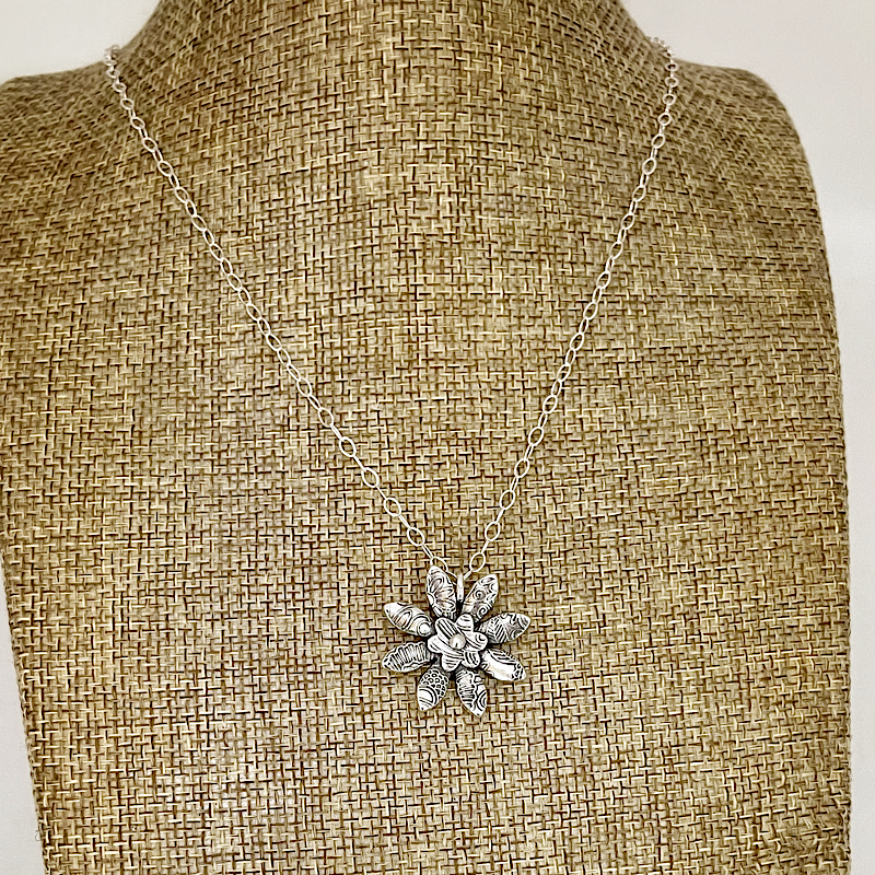 Silver necklace with a floral pendant on a mannequin bust.