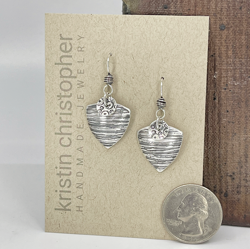 Silver triangle-shaped earrings on a 'Kristin Christopher' card with a quarter for scale.