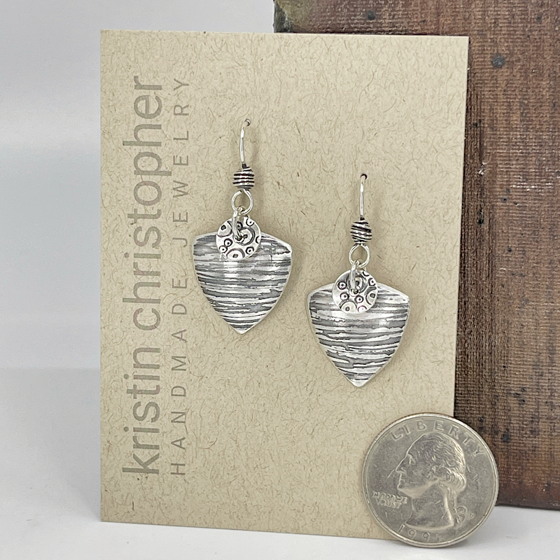 Silver triangle-shaped earrings on a 'Kristin Christopher' card with a quarter for scale.