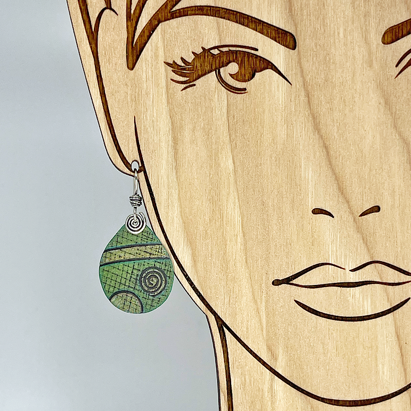Wooden face with a green earring on a gray background