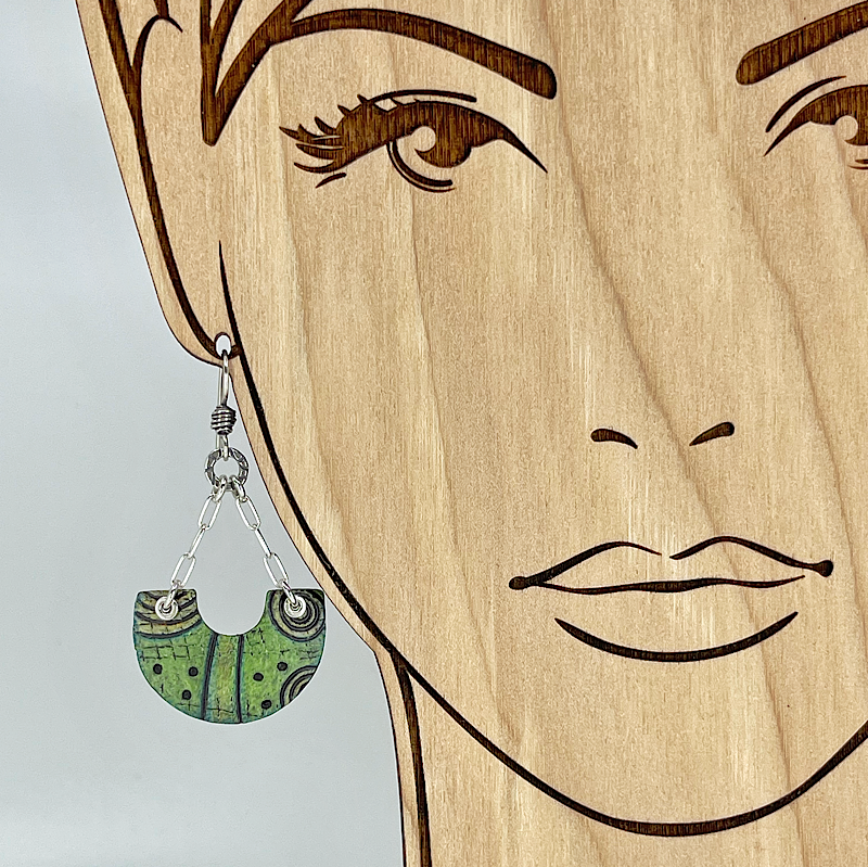 Green, black, and silver earrings shown on a model for scale