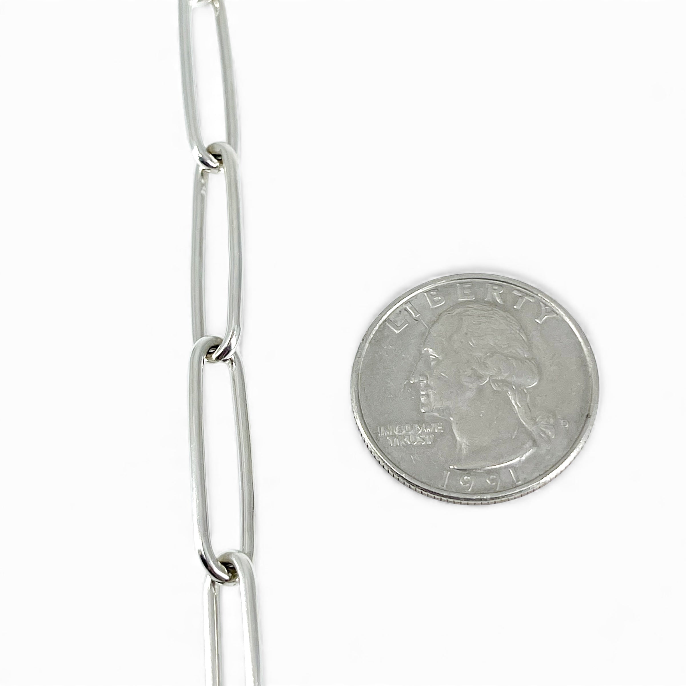 Sterling silver chain bracelet next to a quarter for size comparison on a white background