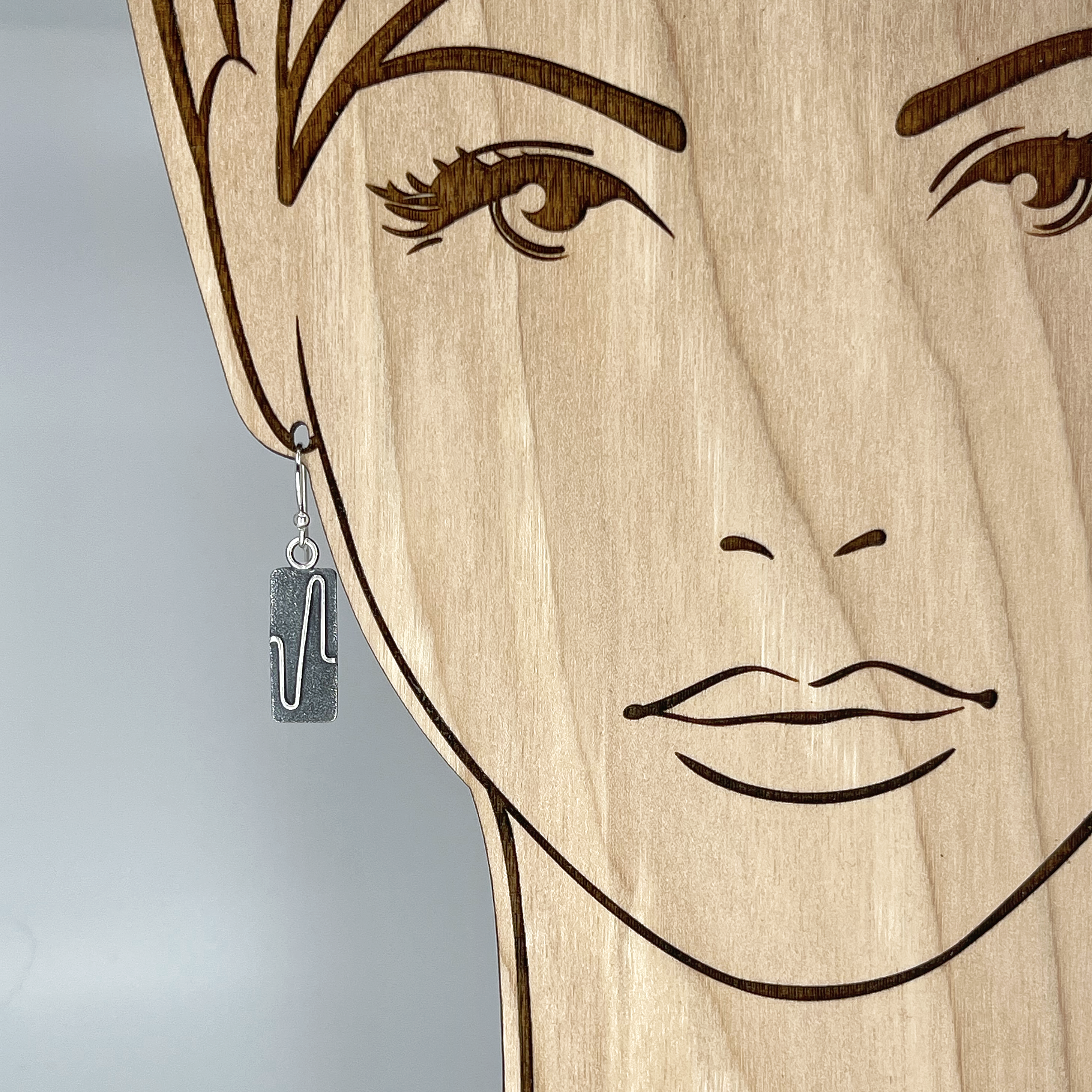 A rectangular sterling silver earring shown on a model