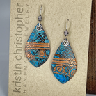 Teardrop-shaped earrings with blue and copper pattern on a 'Kristin Christopher' card.