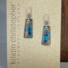 Pair of blue and copper patterned earrings on a textured surface with 'Kristin Christopher Handmade Jewelry' branding.