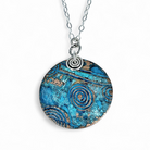 Front view of circular copper blue patina pendant with sterling silver chain and accents