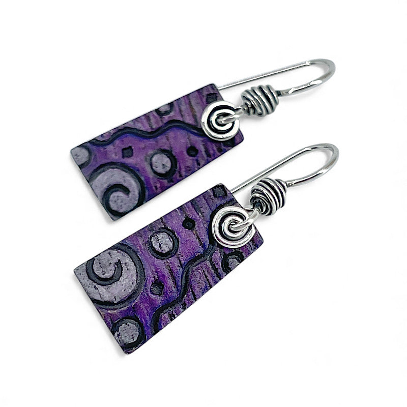 Pair of earrings with purple pattern and silver spirals on a white background